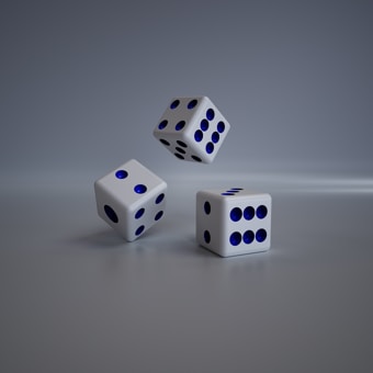 Three white dice with blue spots are on a smooth, reflective surface. One die is in mid-air while the other two are resting on the surface.