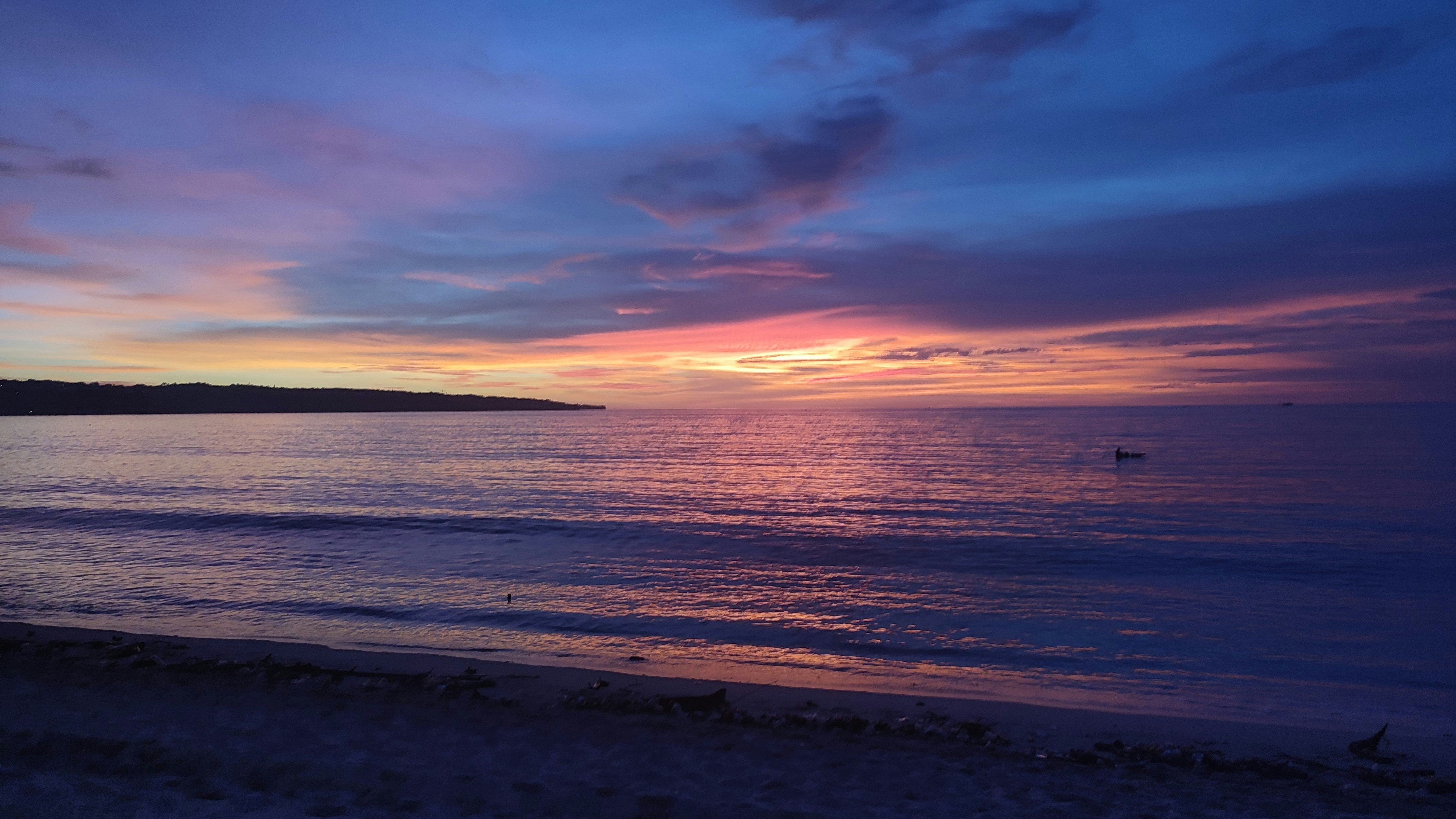 a sunset on a beach with a boat in the water