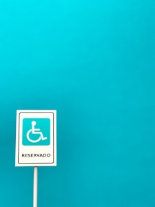 A vertical sign with a white background and a blue symbol of a person in a wheelchair, indicating accessibility, with the word 'Reservado' written below. The sign is set against a solid turquoise blue background.