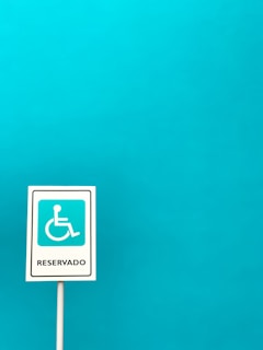 A vertical sign with a white background and a blue symbol of a person in a wheelchair, indicating accessibility, with the word 'Reservado' written below. The sign is set against a solid turquoise blue background.