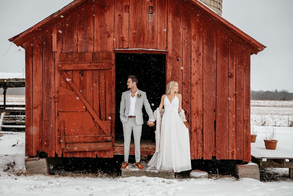 a bride and groom standing in front of a red barn