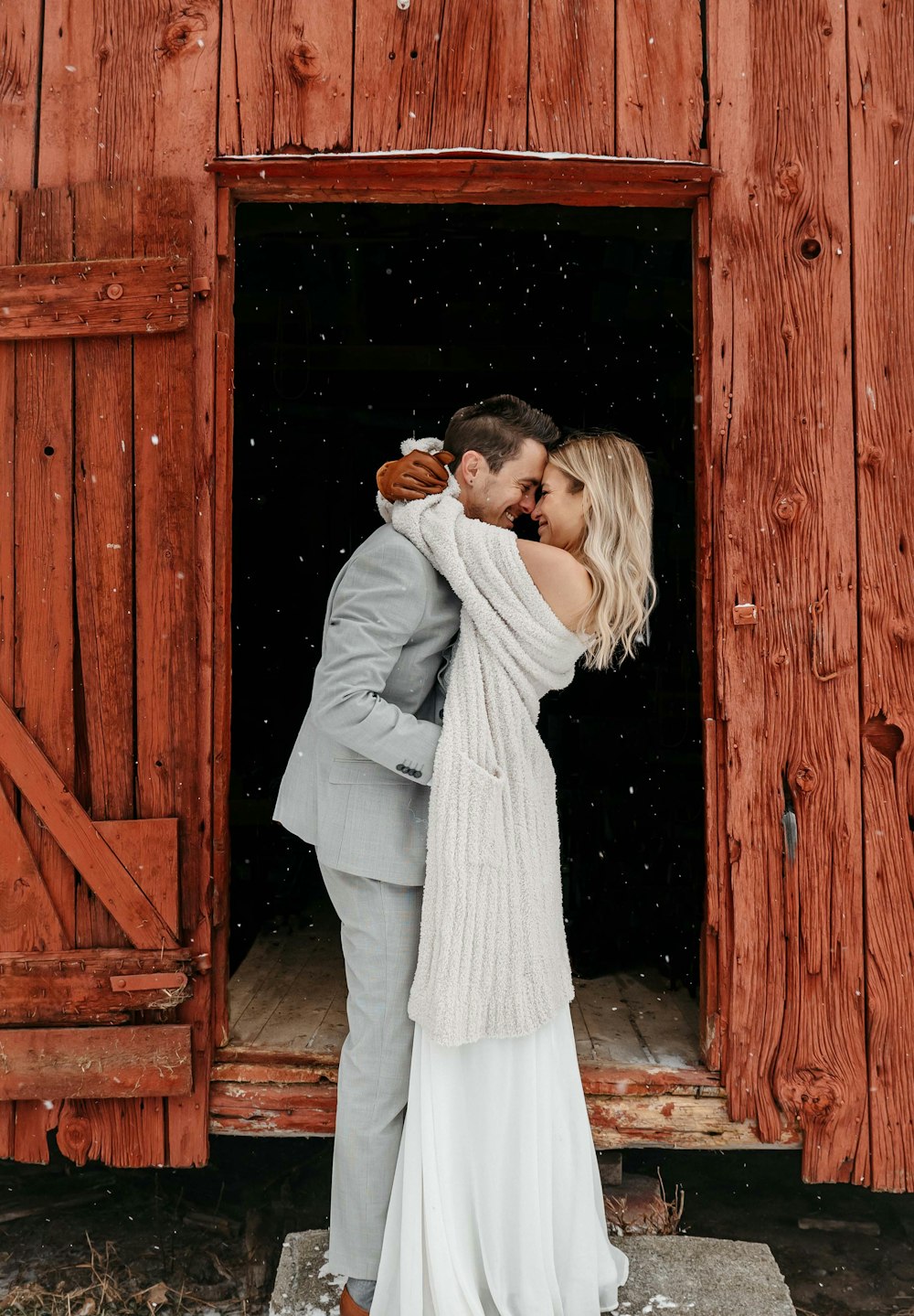 Una novia y un novio se abrazan frente a un granero rojo