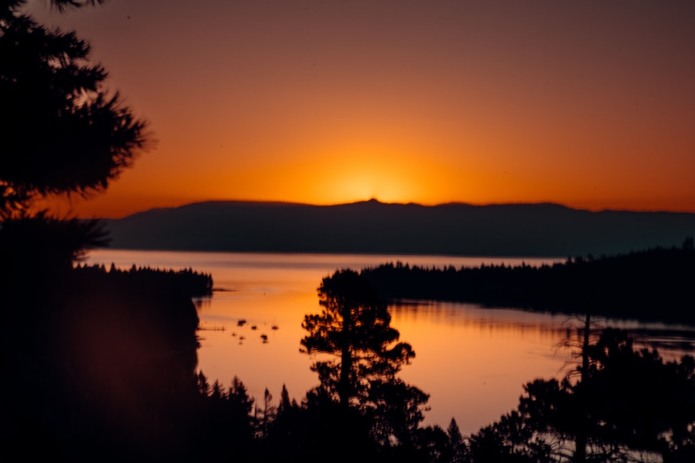 the sun is setting over a lake surrounded by trees