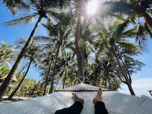 A model lounging in a hammock under palm trees, wearing a crisp white linen shirt with rolled-up sleeves.