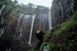 a person sitting on a rock in front of a waterfall