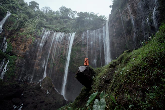 a person sitting on a rock in front of a waterfall