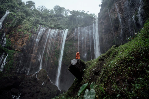 a person sitting on a rock in front of a waterfall