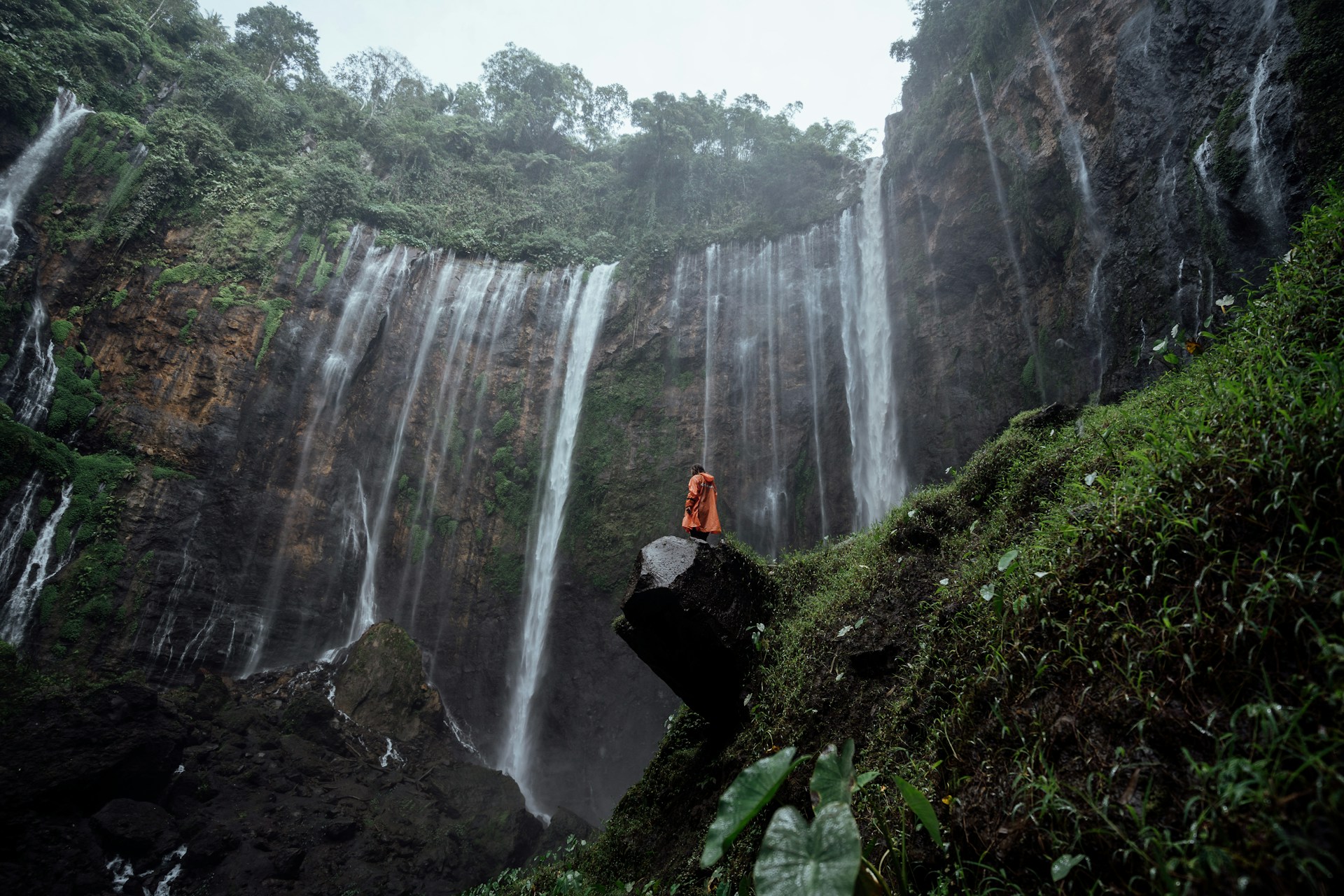 a person sitting on a rock in front of a waterfall