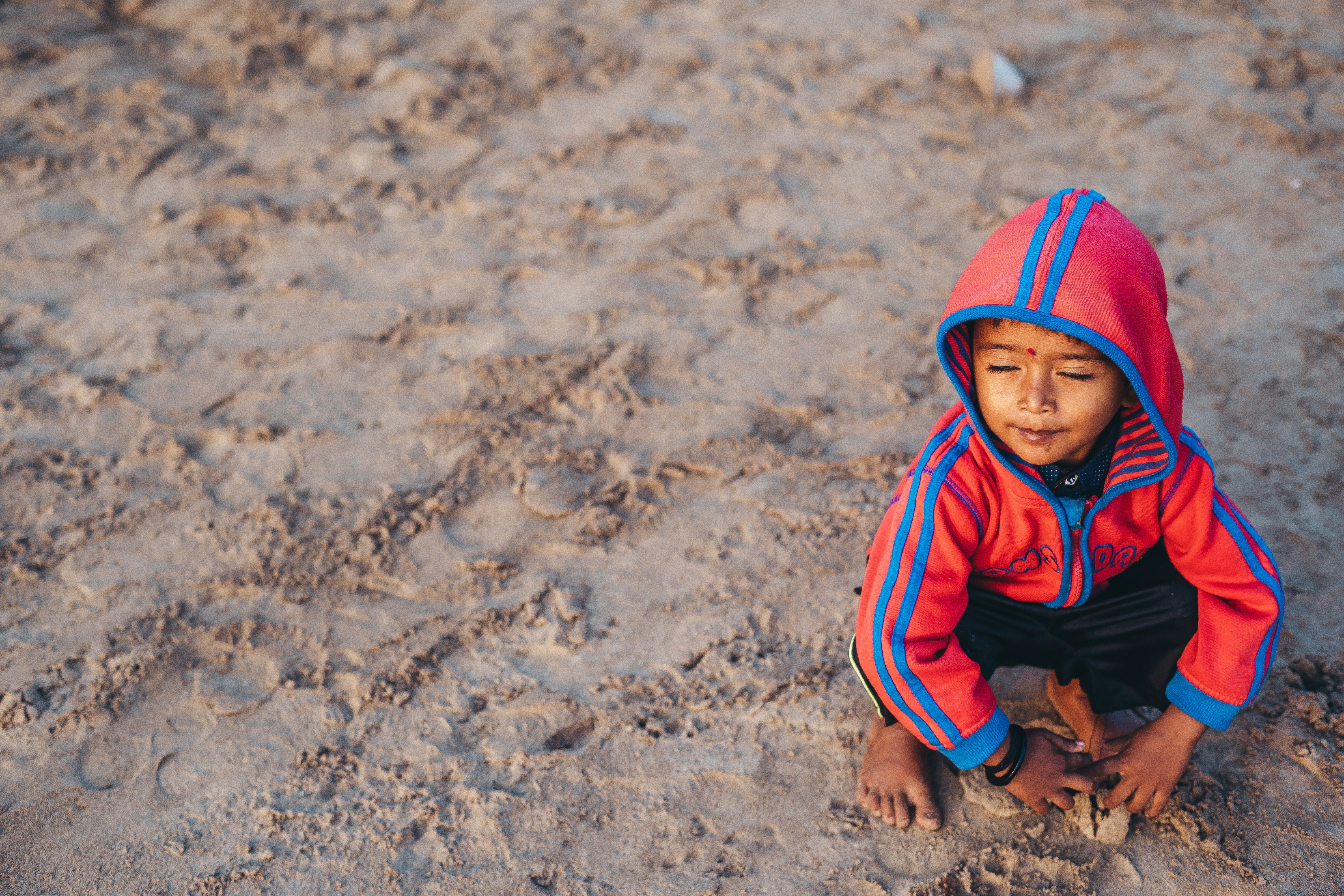 a young boy sitting on the ground in the sand