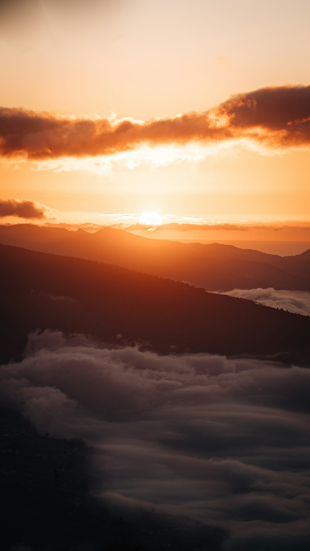 the sun is setting over the clouds in the mountains