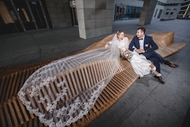 a bride and groom sitting on a wooden bench