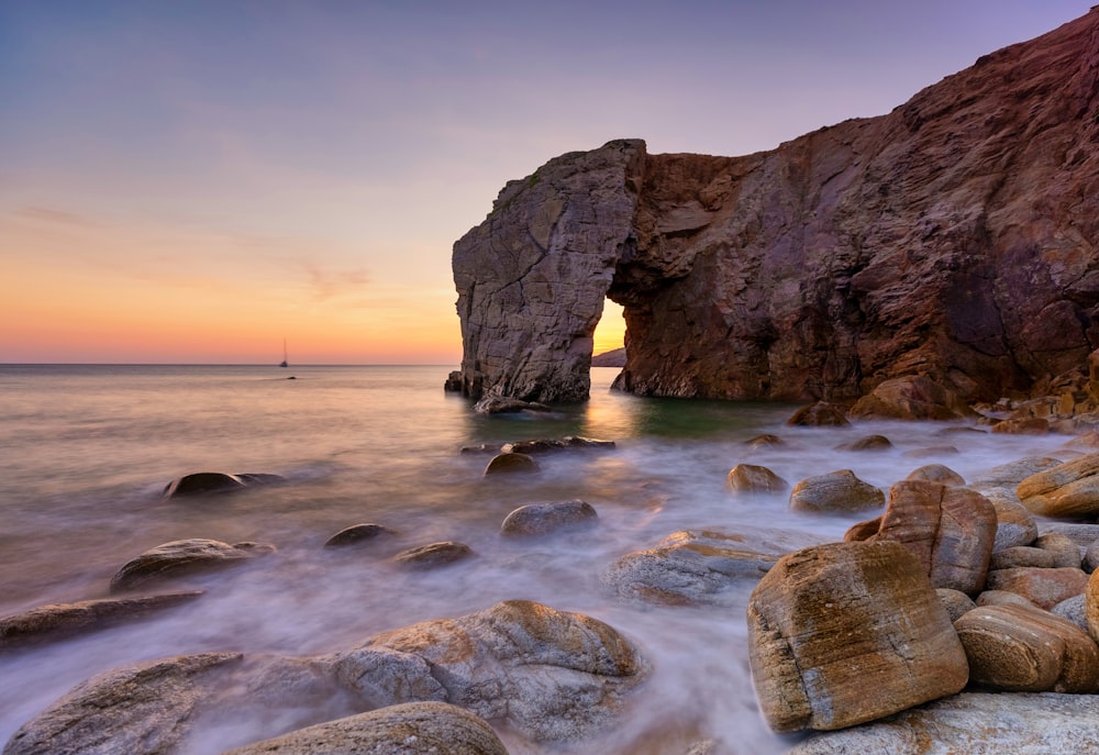 a rocky beach with a rock formation in the water