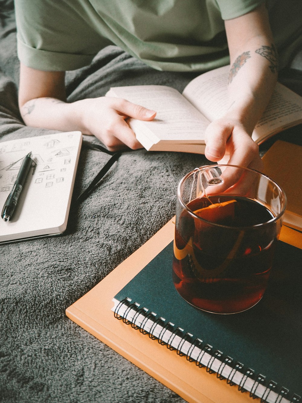 a person sitting on a bed with a book and a drink