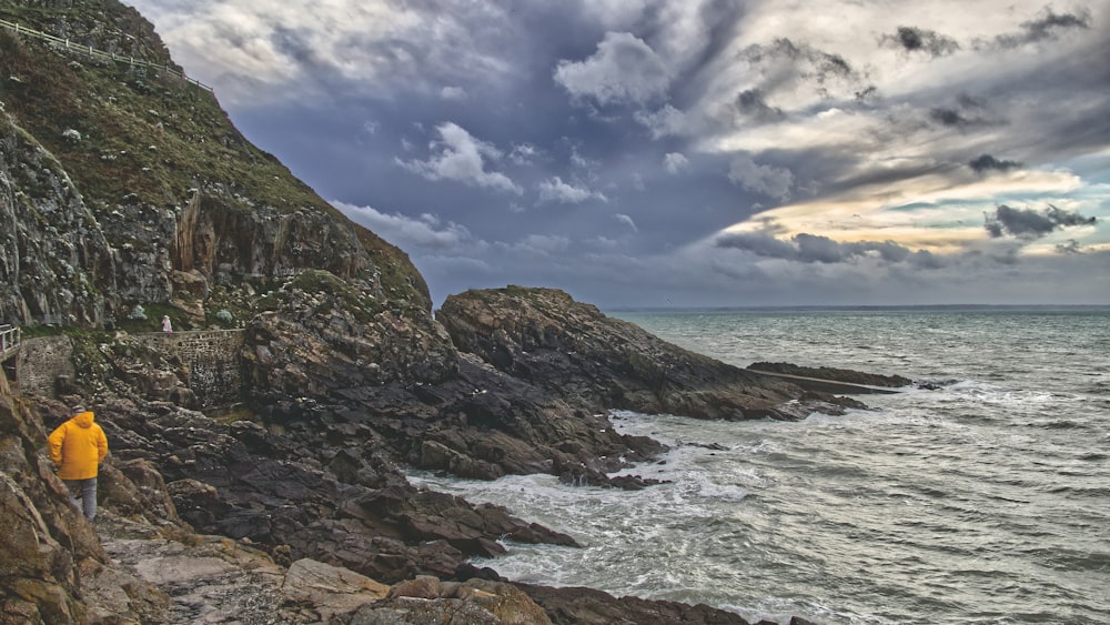 a man standing on a rocky cliff next to the ocean