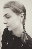 A grayscale portrait of a woman with her hair styled in a braid. She is wearing hoop earrings and a textured black top with subtle patterns. Her eyes are closed, giving a serene and introspective expression.