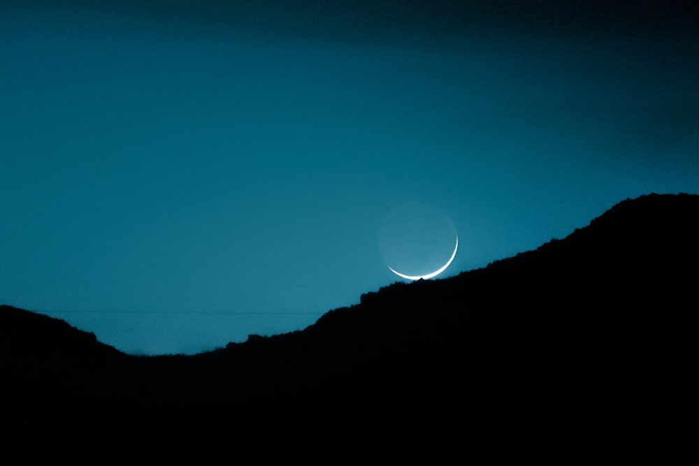 the moon is seen in the sky over a mountain