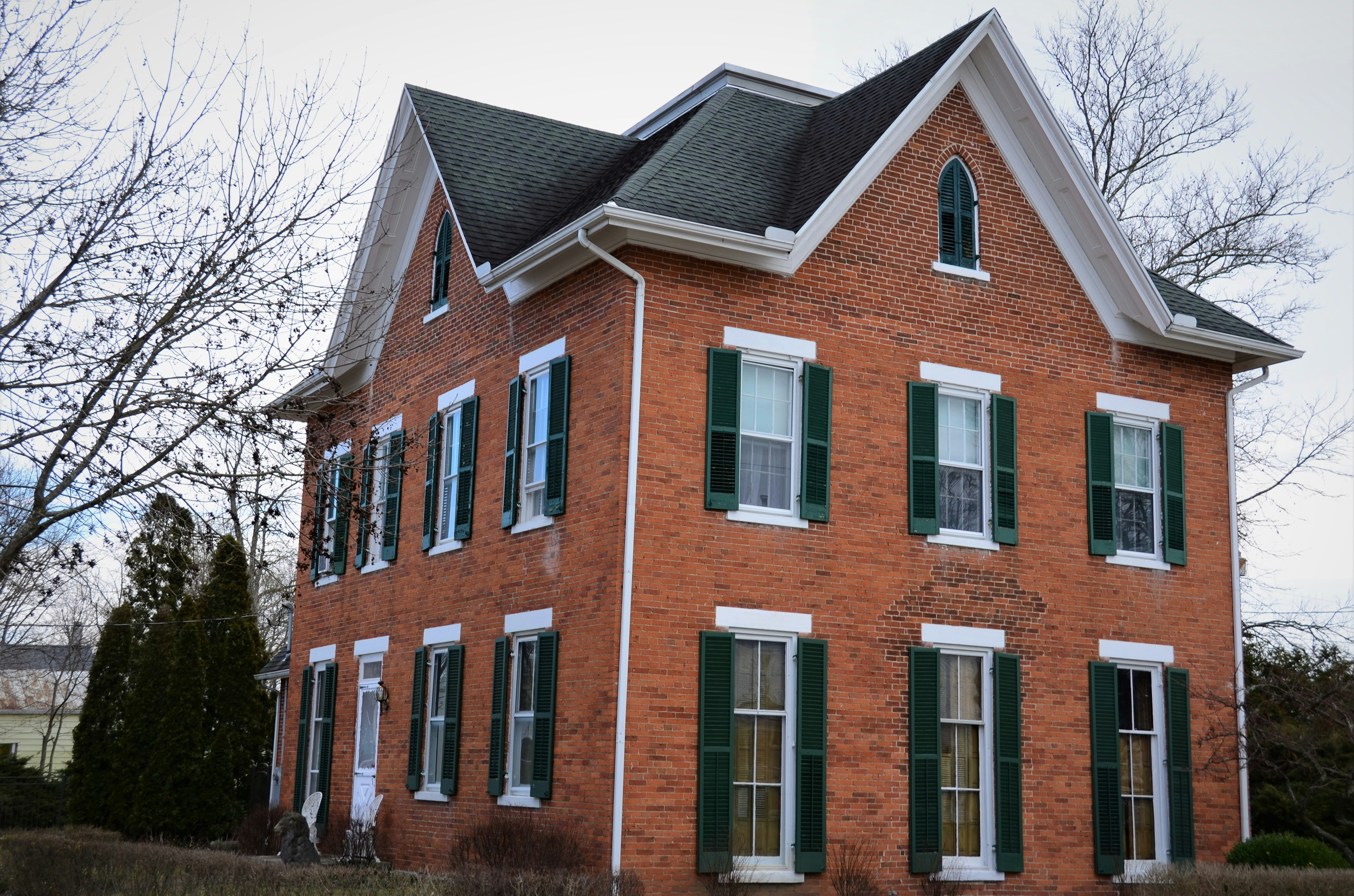 A red brick house with green shutters and a black roof photo Free