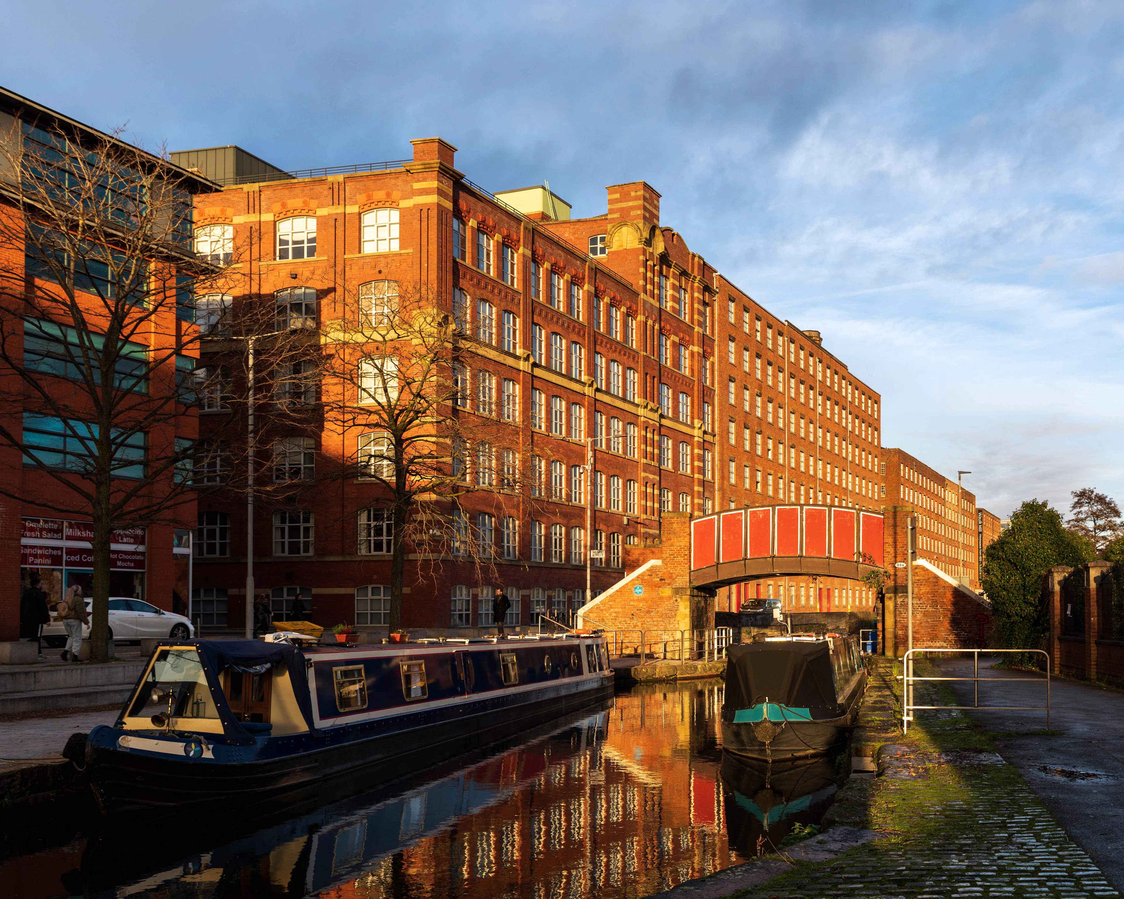 Narrowboats moored on a canal beside red-brick Victorian warehouses at golden hour
