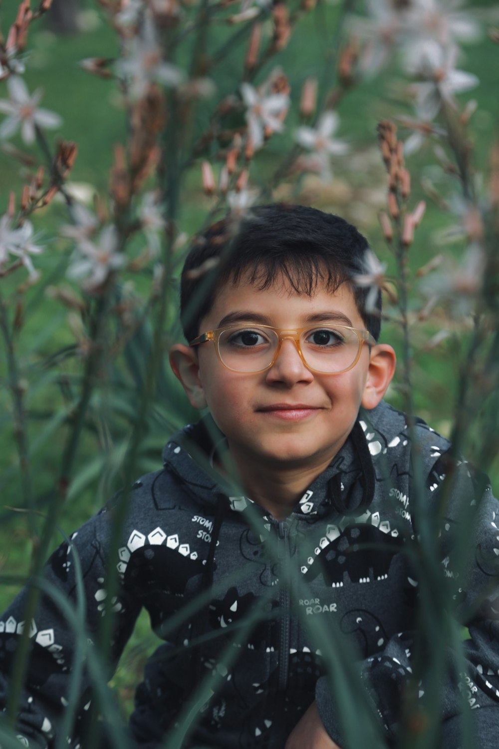a young boy wearing glasses standing in a field of flowers