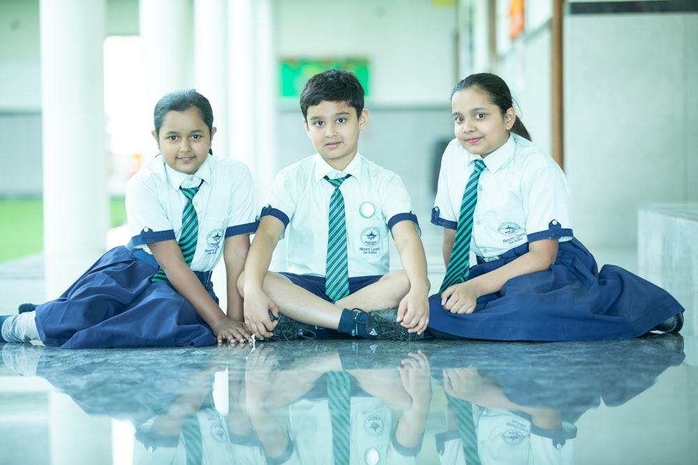 three young children sitting on the ground wearing ties
