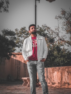A stylish man wearing a casual jacket and jeans, smiling confidently outdoors.