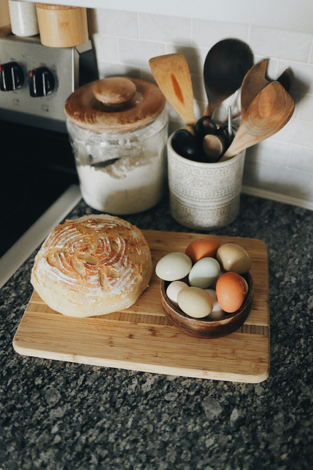a wooden cutting board topped with a loaf of bread next to eggs