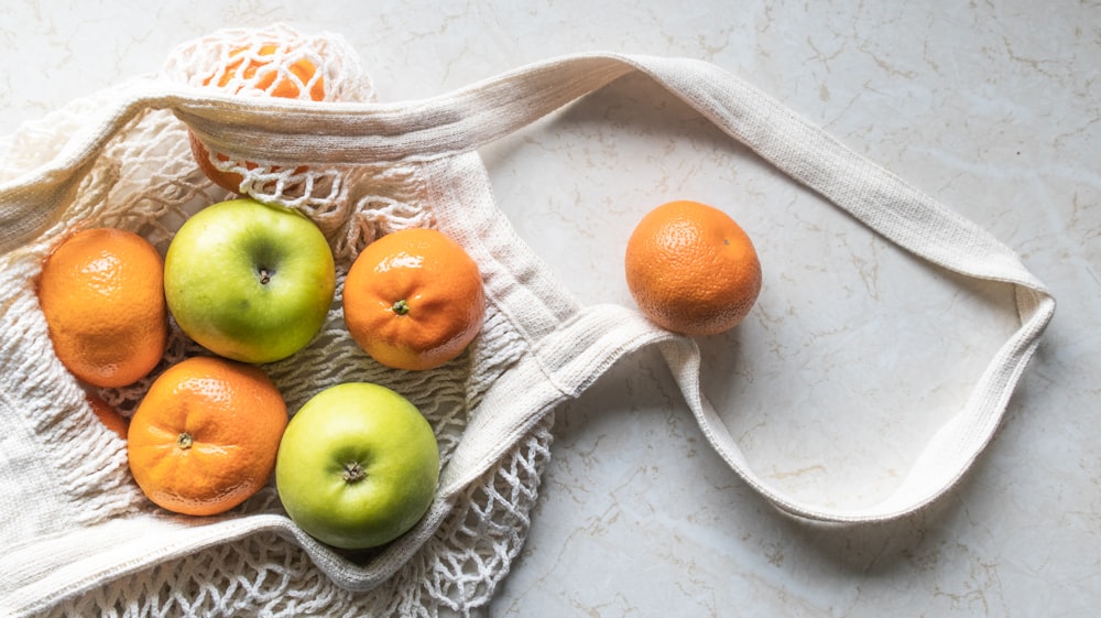 a white bag filled with oranges and apples