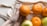A hand is holding an orange while other oranges and a green apple rest in a reusable mesh bag. The scene suggests an eco-friendly approach to carrying fresh fruit.