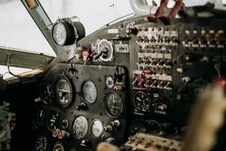 A detailed view of an aircraft cockpit featuring various dials, gauges, switches, and controls. The panel is densely packed with instruments, some with colored markers and wiring running through it.