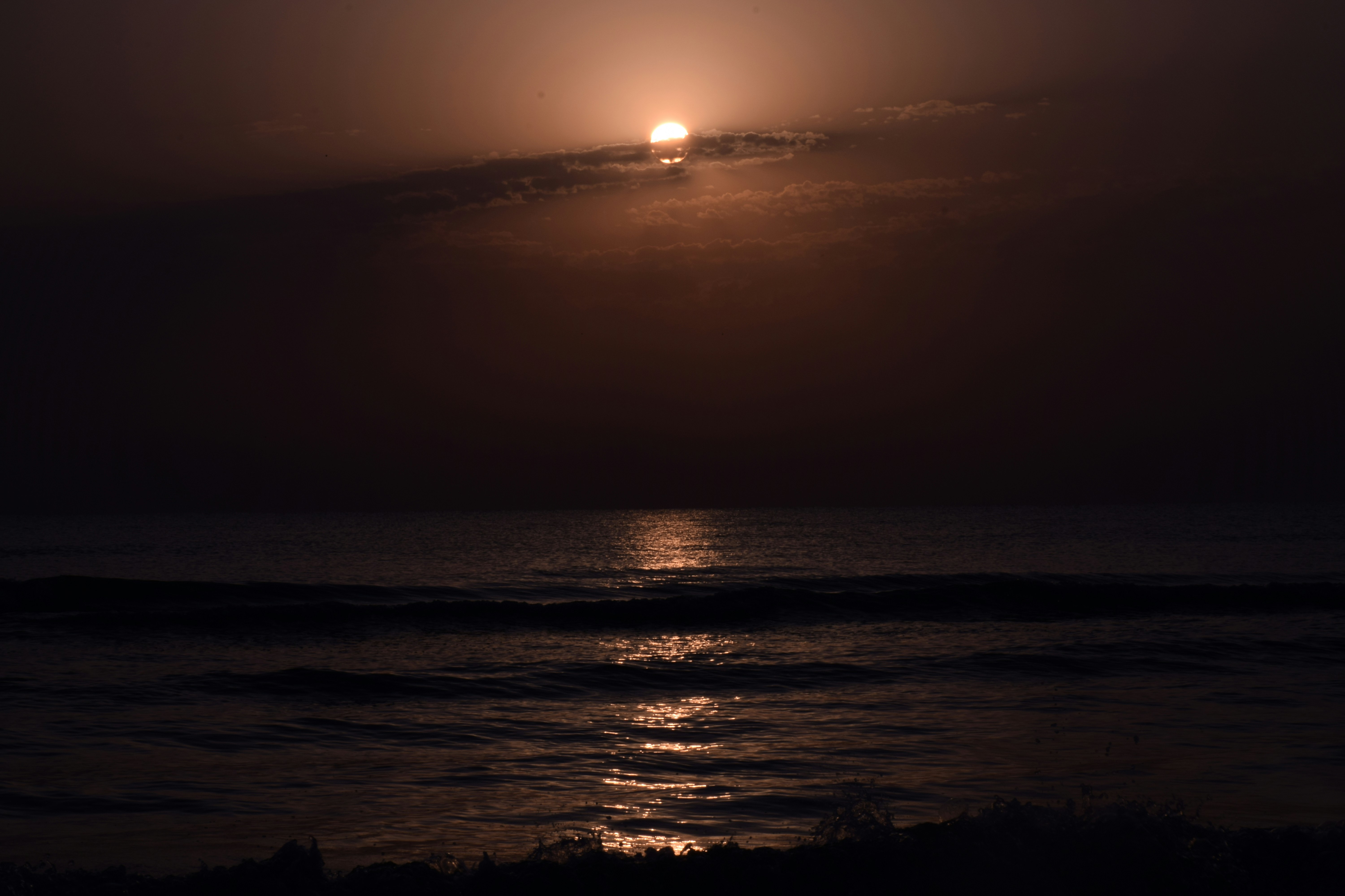 the sun is setting over the ocean on a cloudy day