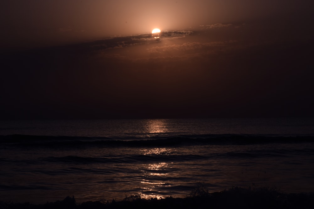 the sun is setting over the ocean on a cloudy day