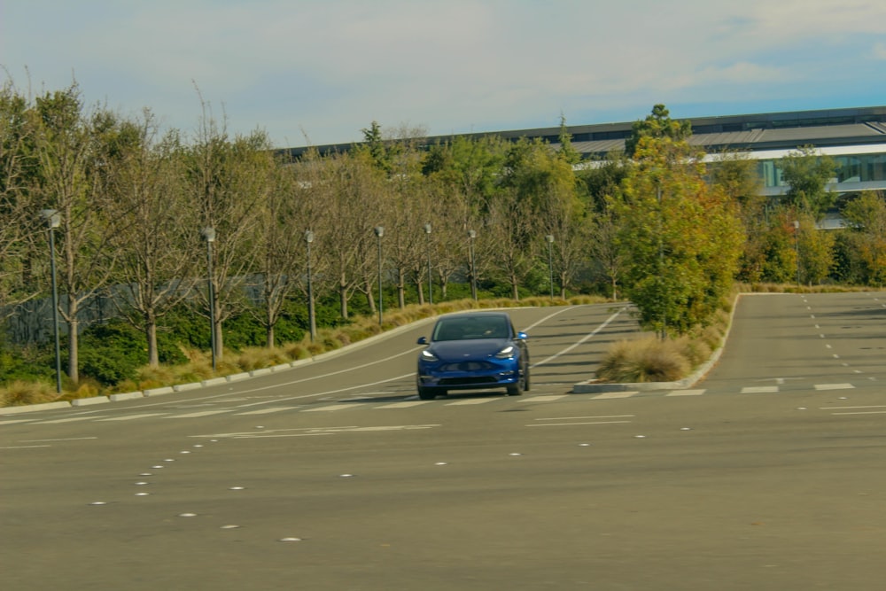 a blue car driving down a street next to trees