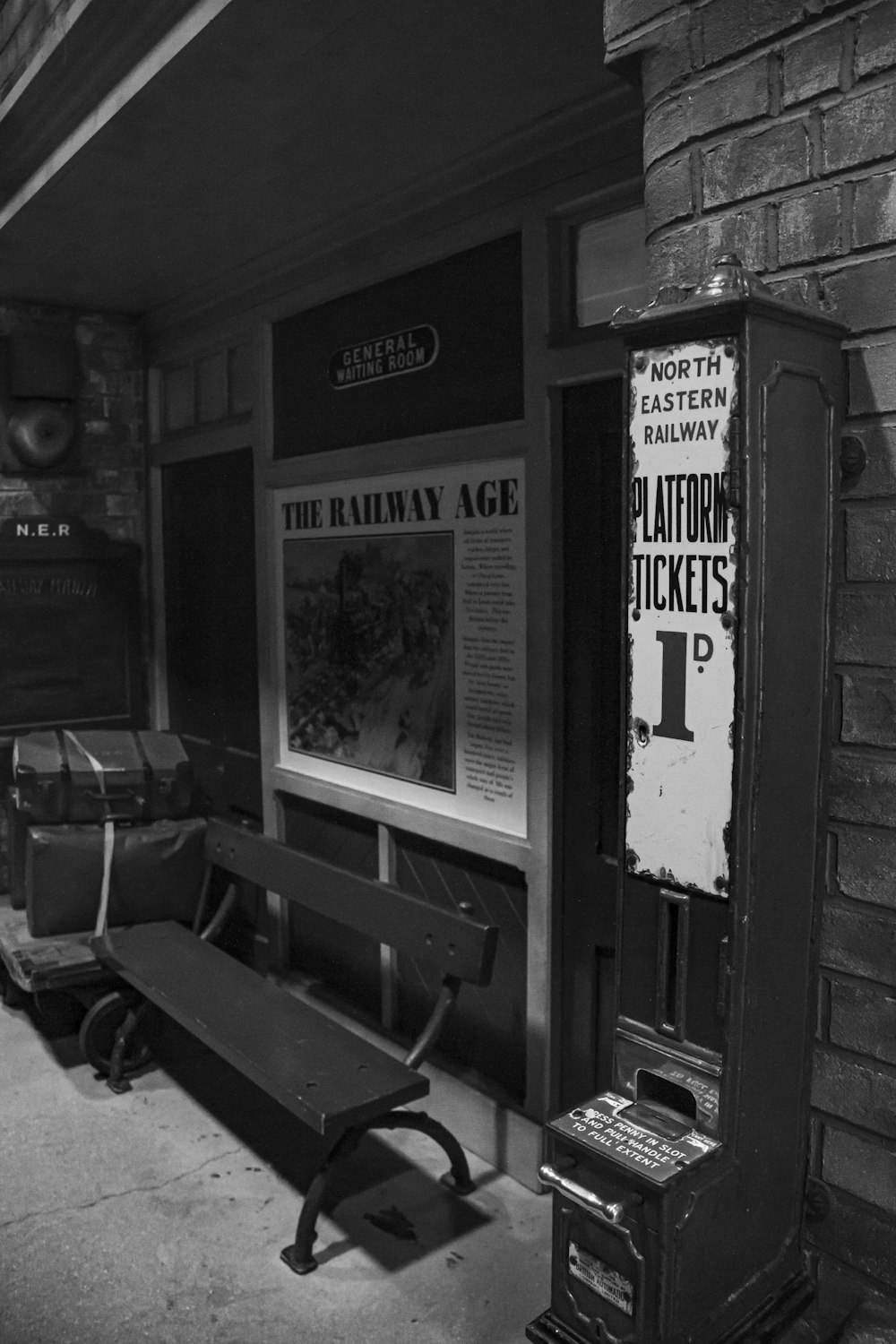 a black and white photo of a bench in front of a ticket booth