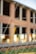 A chain-link fence topped with barbed wire is in the foreground, slightly out of focus. Behind the fence, a brick building under construction or undergoing renovation is visible, with large open windows and unfinished surfaces.