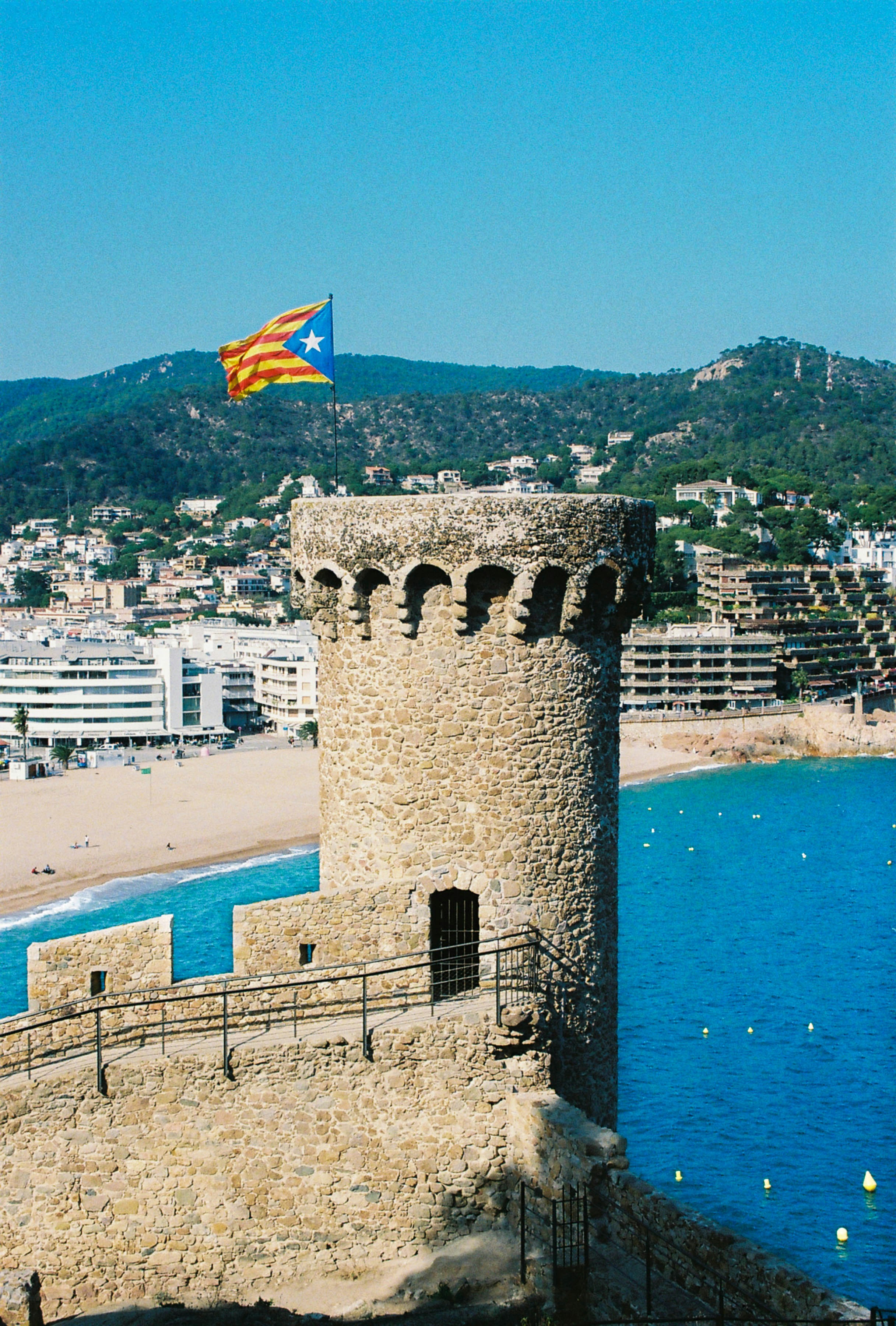 a flag flying on top of a stone tower next to a body of water