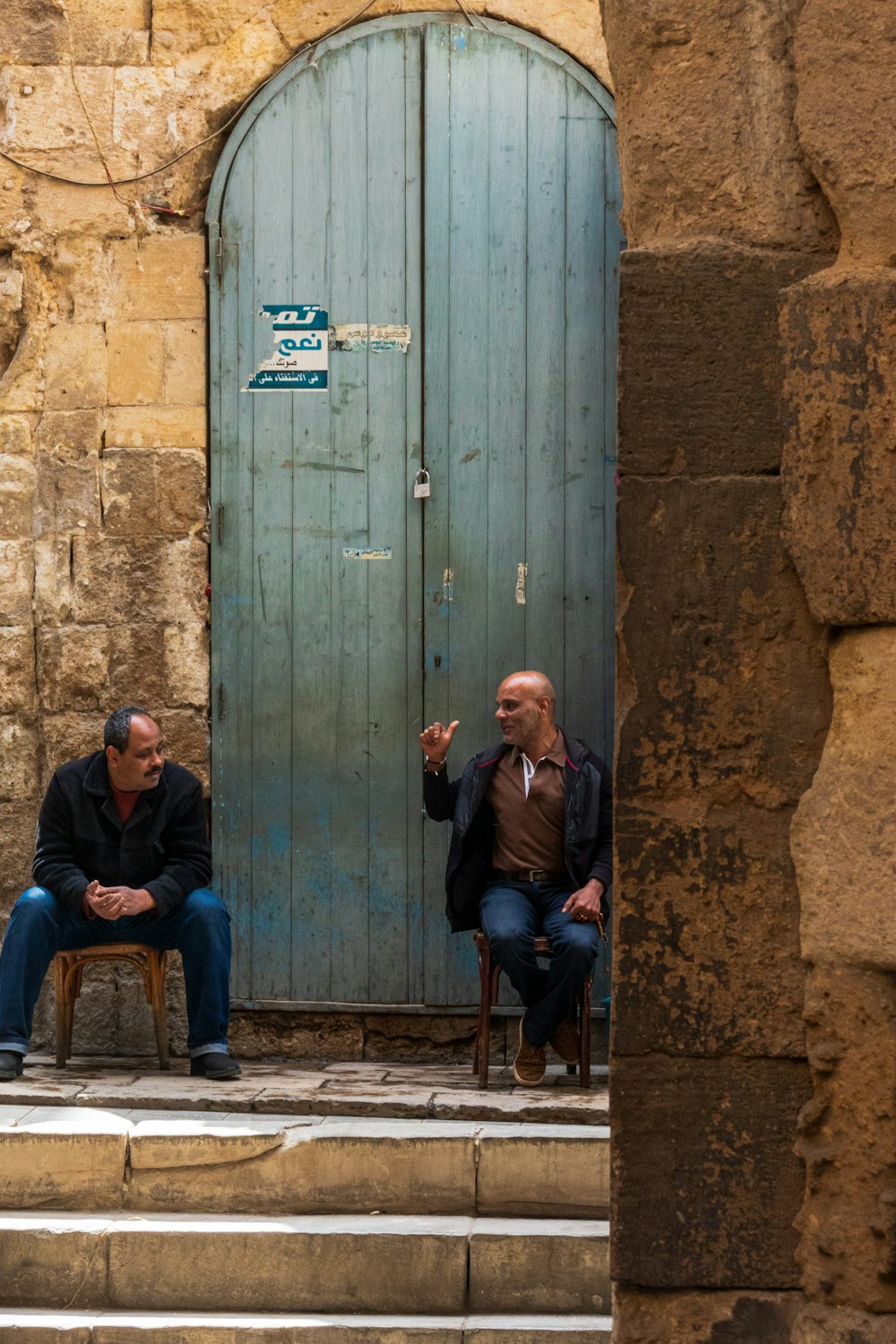 a couple of men sitting next to each other in front of a blue door