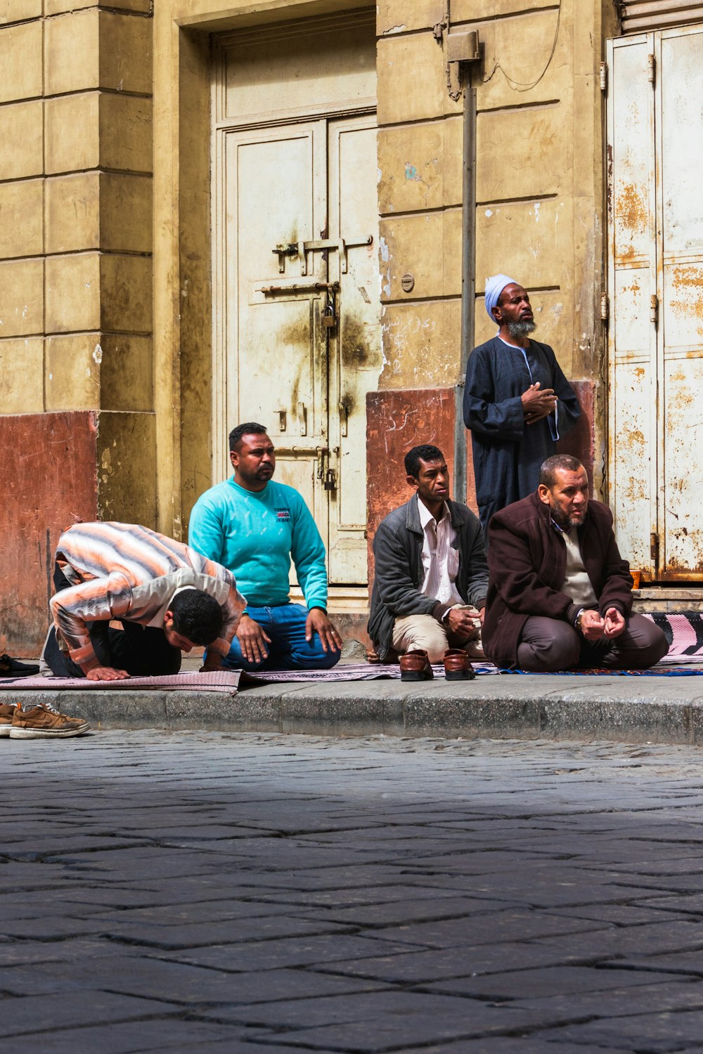 a group of men sitting on the ground in front of a building