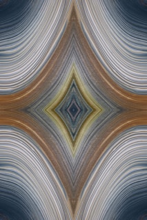 An abstract design featuring a symmetrical, kaleidoscopic pattern with curved lines converging towards a central diamond shape. The lines exhibit a variety of textures and gradients, creating an intricate visual effect reminiscent of layered fabric or natural formations.