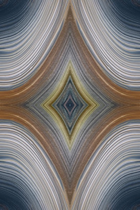 An abstract design featuring a symmetrical, kaleidoscopic pattern with curved lines converging towards a central diamond shape. The lines exhibit a variety of textures and gradients, creating an intricate visual effect reminiscent of layered fabric or natural formations.