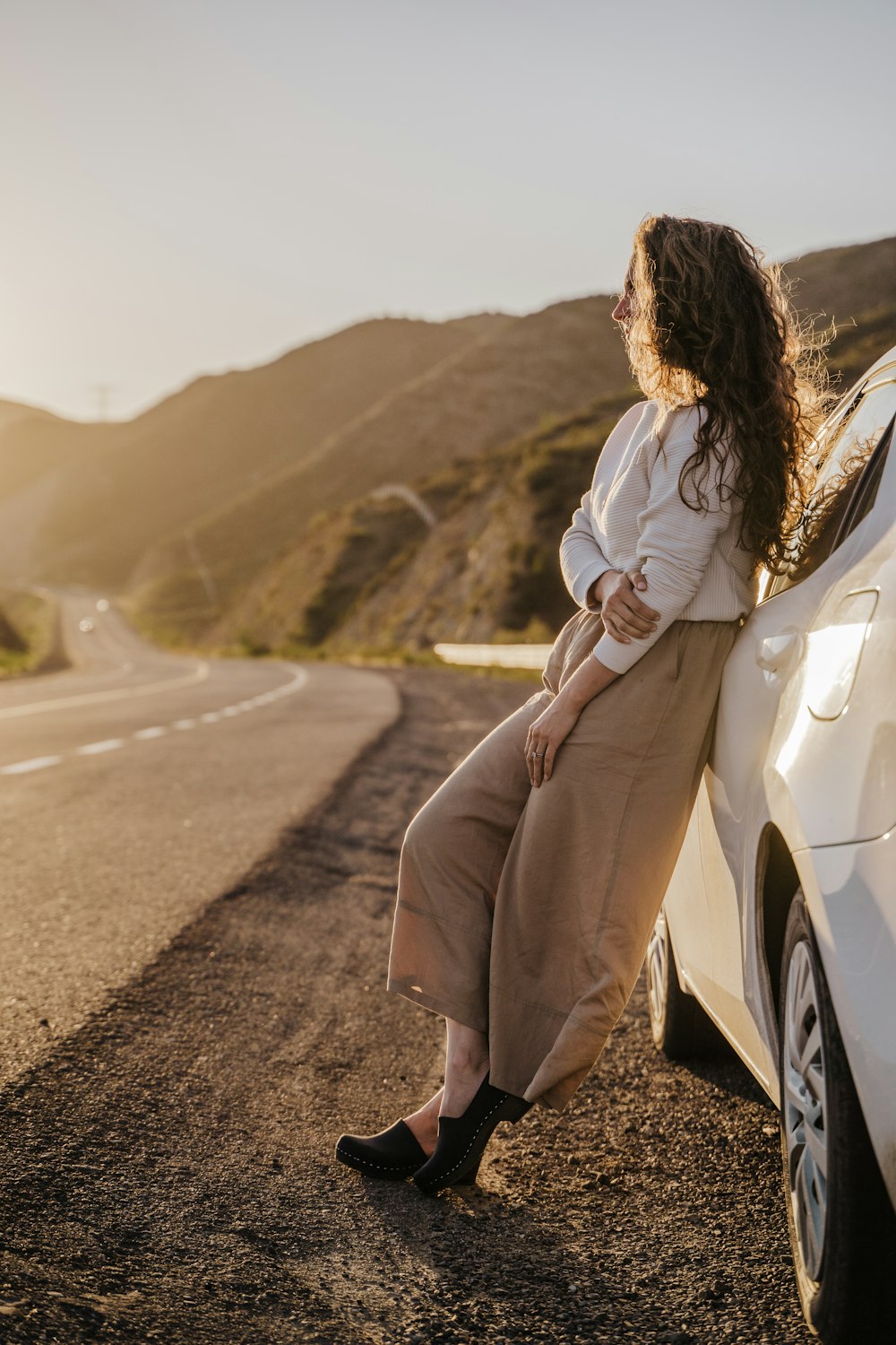 a woman leaning against a car on the side of the road