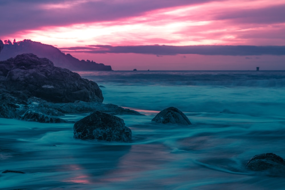 a sunset over the ocean with rocks in the foreground