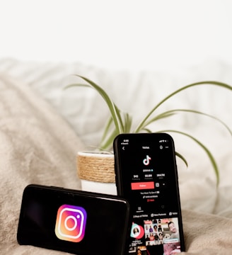 two cell phones sitting on top of a bed next to a plant