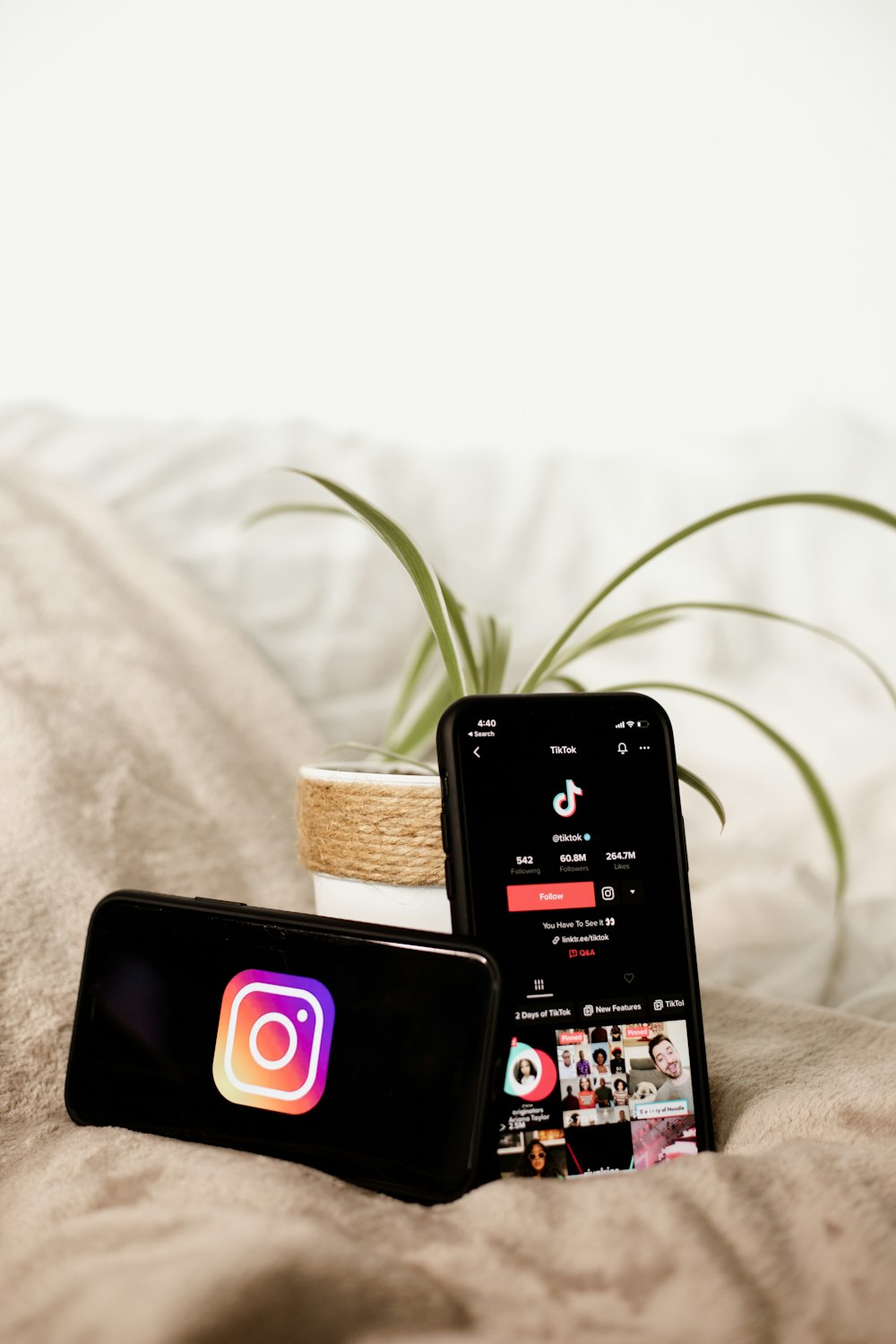 two cell phones sitting on top of a bed next to a plant