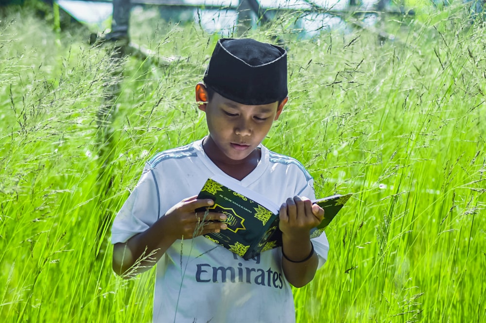 a young boy standing in a field looking at a book
