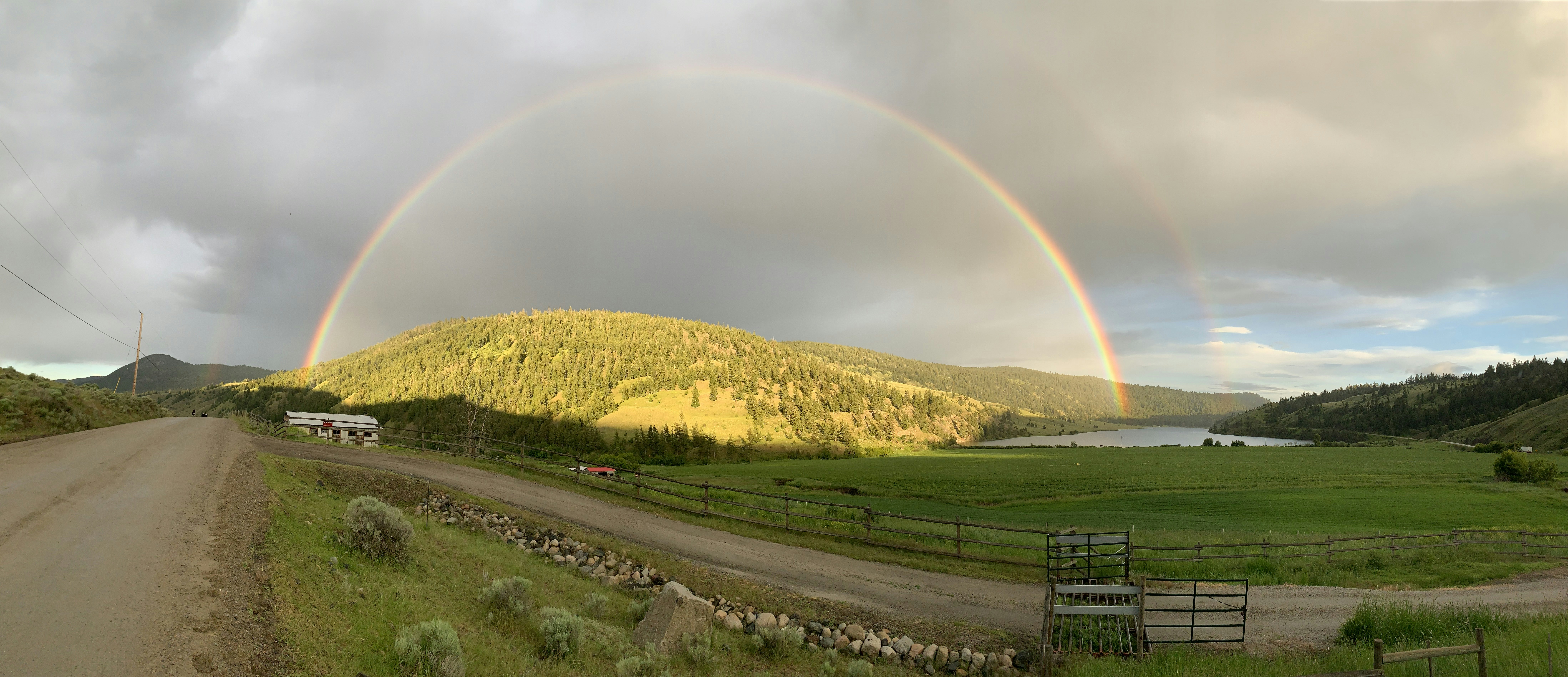 two rainbows in the sky over a dirt road