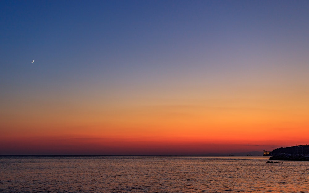 the sun is setting over the ocean with a boat in the water