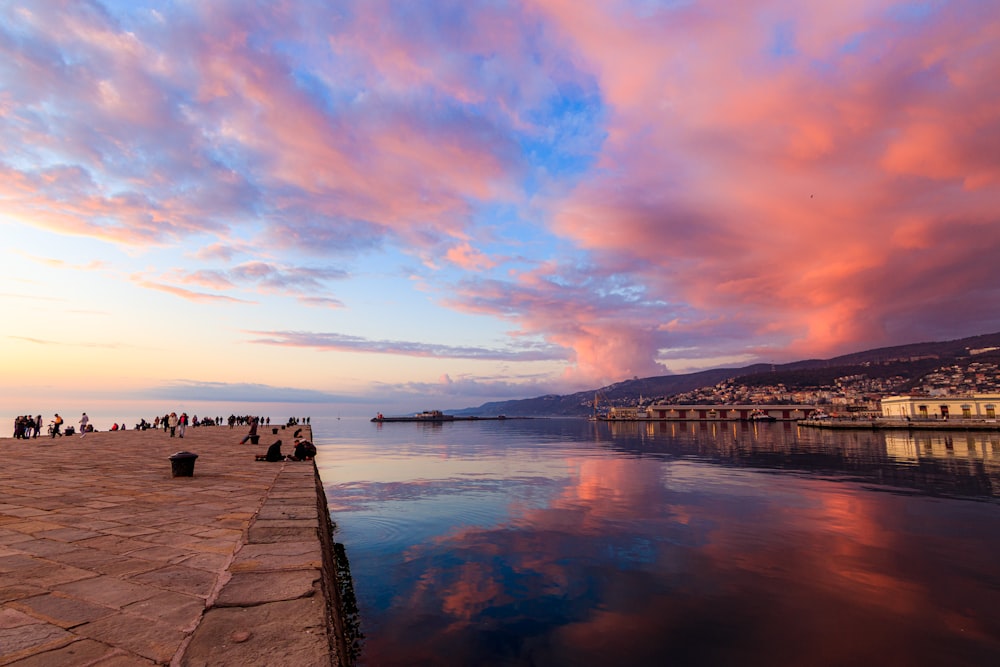 a group of people standing on a pier next to a body of water