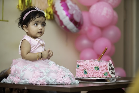 a little girl sitting in front of a pink cake