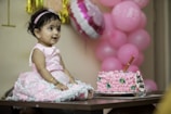 a little girl sitting in front of a pink cake