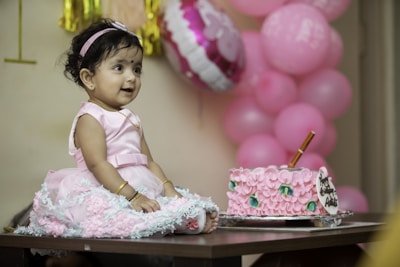 a little girl sitting in front of a pink cake
